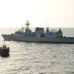 HMCS Charlottetown looms in the background as a boarding party team comes alongside a dhow boat after a ScanEagle Unmanned Arial Vehicle spotted a suspicious cargo exchange between the boat and another skiff.