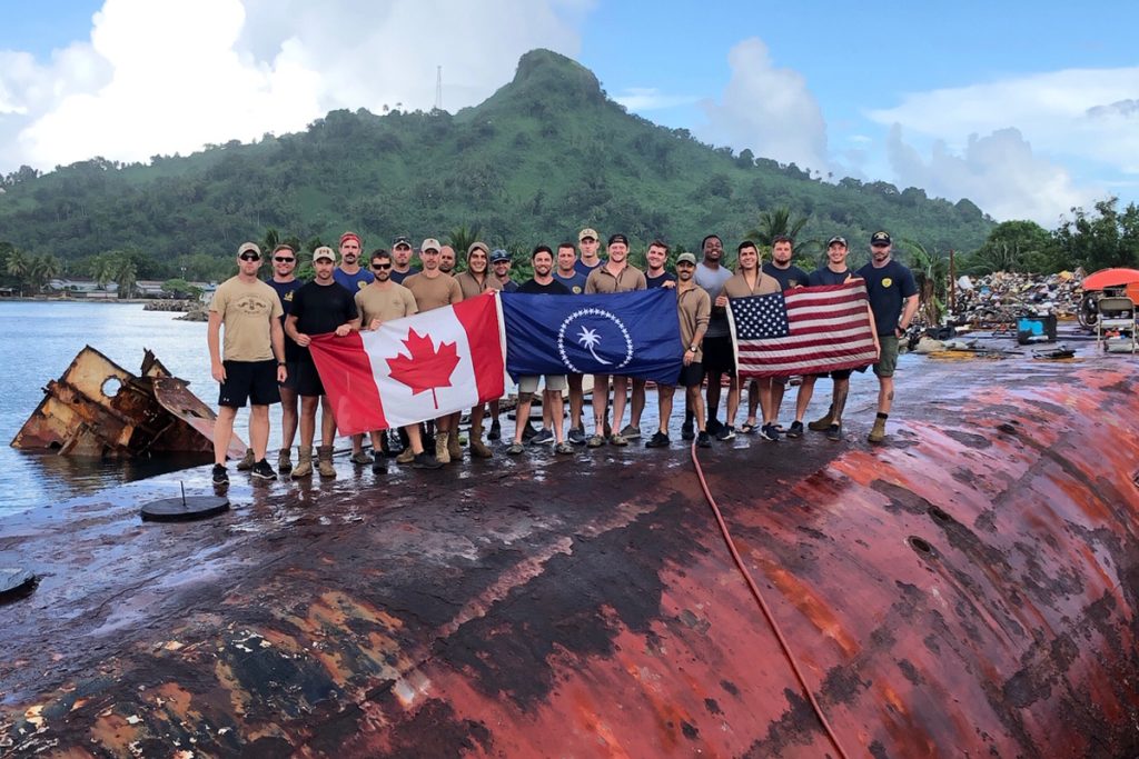 Members of the Fleet Diving Unit (Pacific) and the United States Navy salvage project gather for a team photo on the hull of the MV Micro Dawn in Weno