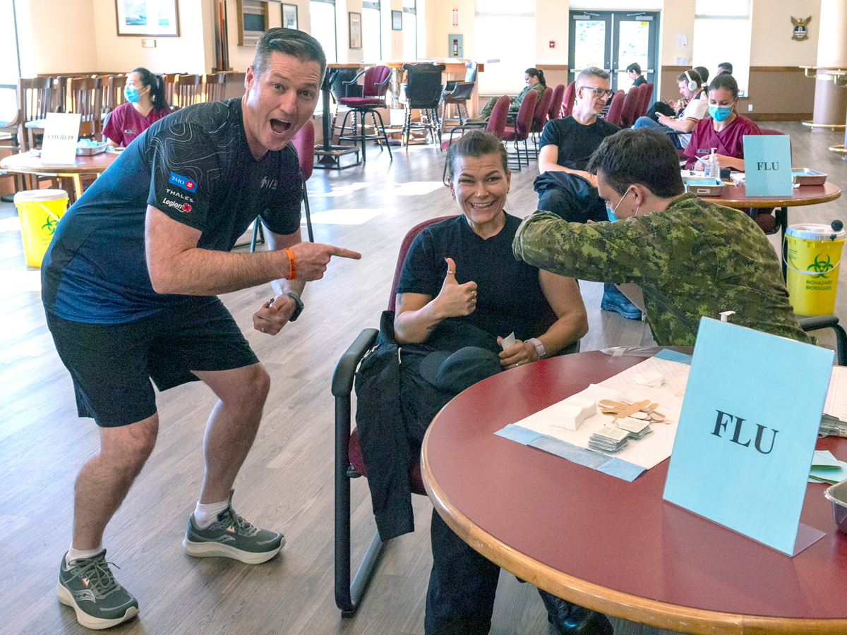 Base Commander Captain (Navy) Kevin Whiteside, Supports Base Chief Petty Officer Susan Frisby receiving immunization shots from the Vaccination Clinic at Wardroom.
