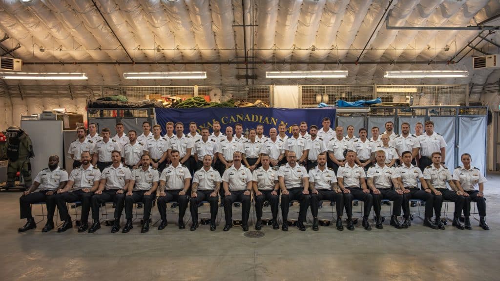 Staff from the Fleet Diving Unit (Pacific)’s (FDU(P)) School of Diving (front row) pose alongside the two new serials of clearance diver students (standing on either side) at the graduation parade for serial CD 0020 (standing, centre).